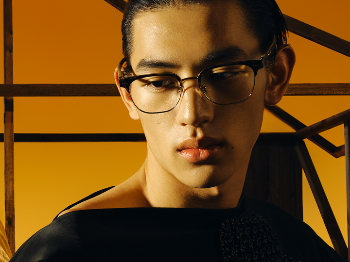 Model wearing MUJOSH optical frames in a warm orange toned editorial portrait